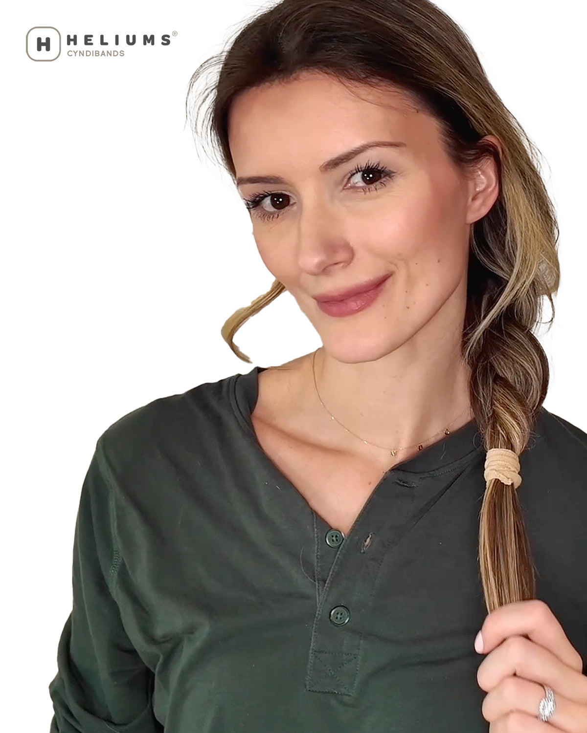 A woman wearing a braid, holding a section of her hair secured with a beige elastic band. The Heliums logo is visible in the top left corner against a white background.