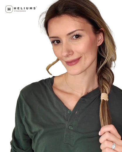 A woman wearing a braid, holding a section of her hair secured with a beige elastic band. The Heliums logo is visible in the top left corner against a white background.