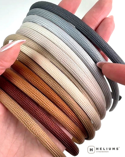 A hand holding a stack of headbands in multiple colors, including dark gray, light gray, cream, tan, brown, and burgundy. The Heliums logo is visible in the bottom right corner.