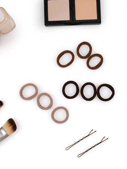 Heliums brown and black Small Seamless Hair Ties shown laying flat next to bobby pins and makeup