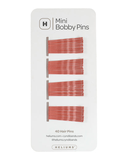 Heliums mini bobby pins in a auburn red hue, packaged on a white card with the Heliums logo at the top.